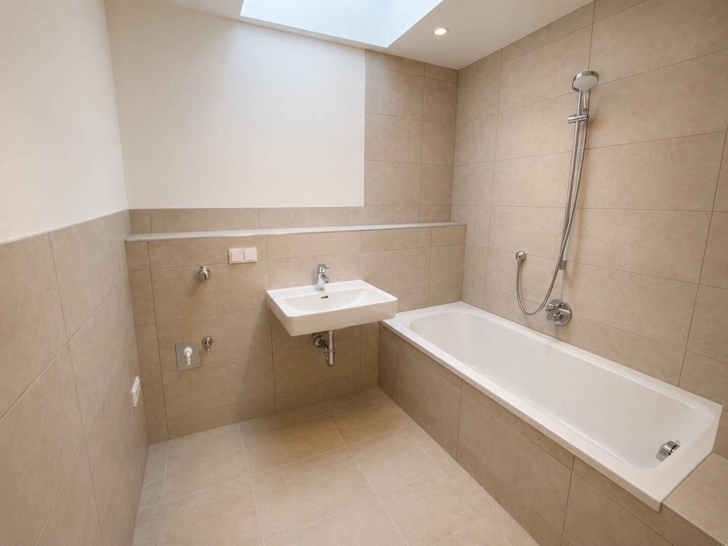 Modernes Badezimmer mit beigefarbenen Fliesen, Badewanne und Waschbecken.