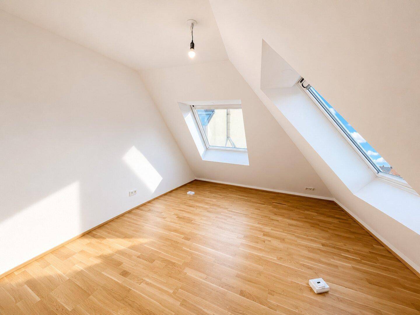 Lichtdurchflutetes Schlafzimmer im Dachgeschoss mit Holzboden und zwei Dachfenstern.