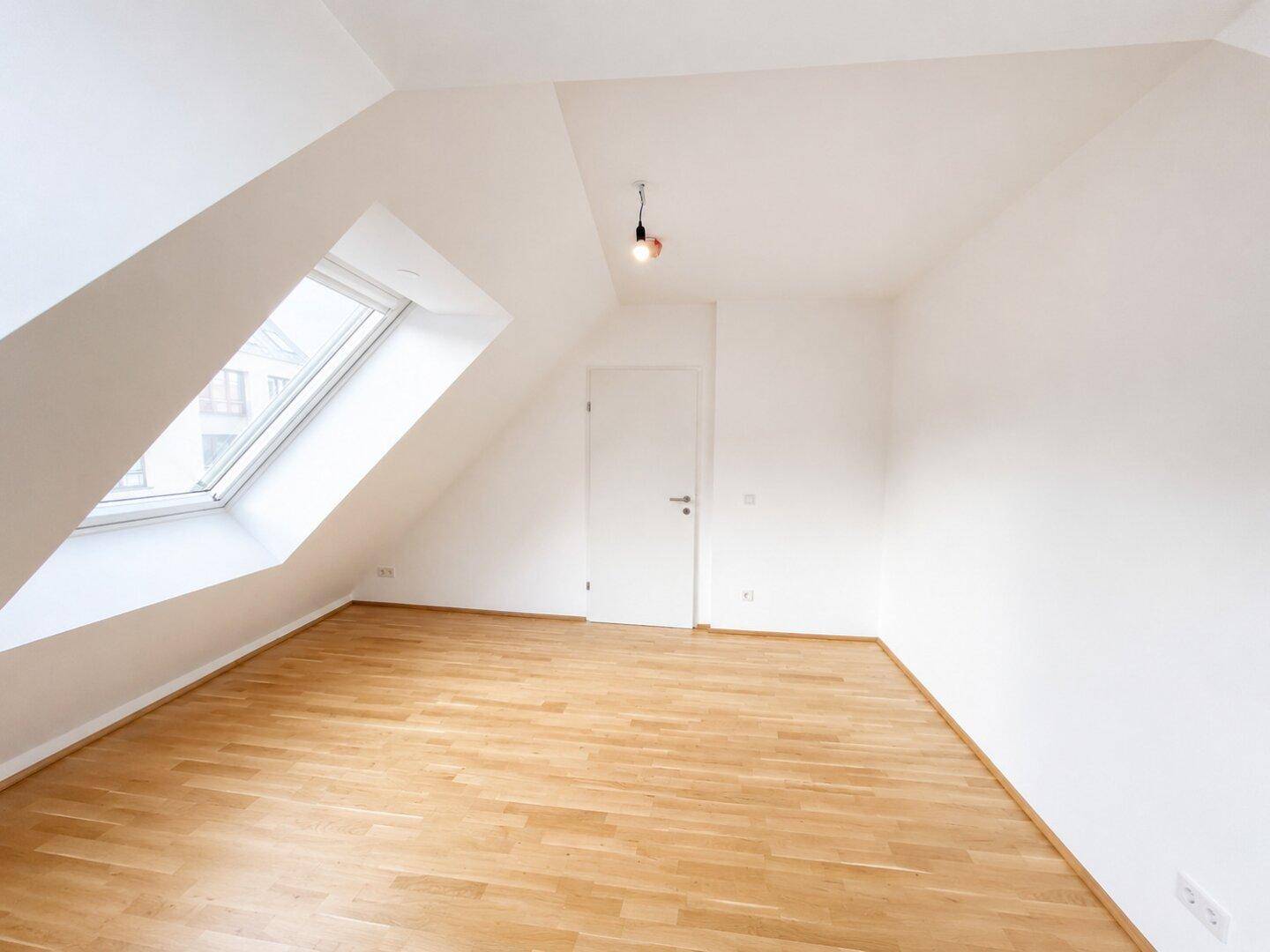 Geräumiges Schlafzimmer im Dachgeschoss mit Holzboden und einem großen Dachfenster.