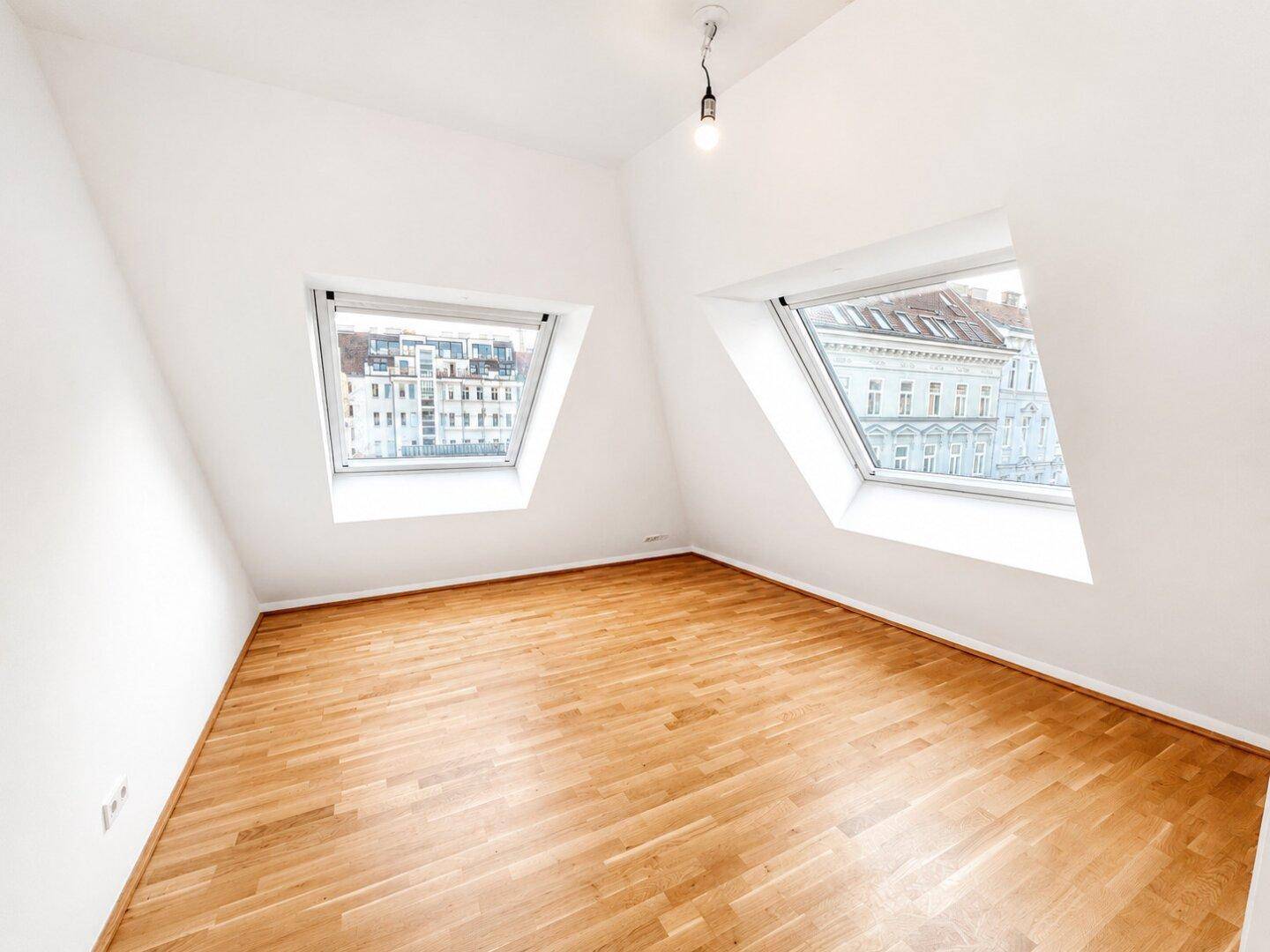 Helles Schlafzimmer im Dachgeschoss mit Holzboden und zwei großen Dachfenstern.