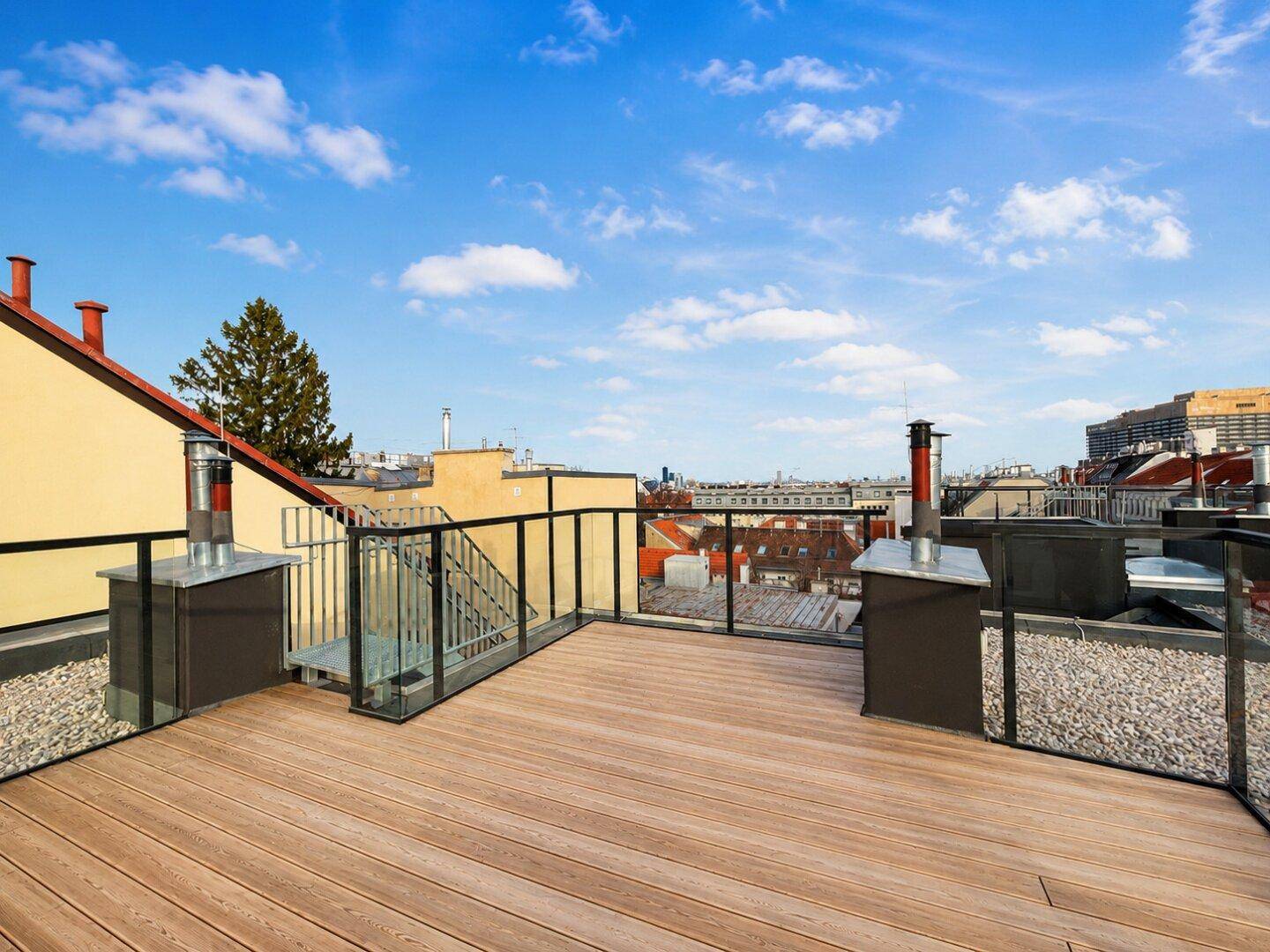 Geräumige Dachterrasse mit Holzboden und Glasgeländer bietet weite Ausblicke über die Stadt.