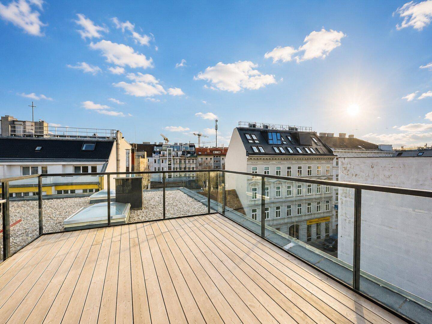 Dachterrasse mit Holzboden und Glasgeländer bei Sonnenuntergang, bietet weite Stadtblicke.