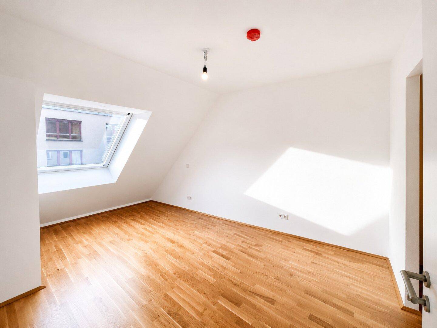 Geräumiges Schlafzimmer im Dachgeschoss mit Holzboden und einem großen Dachfenster.