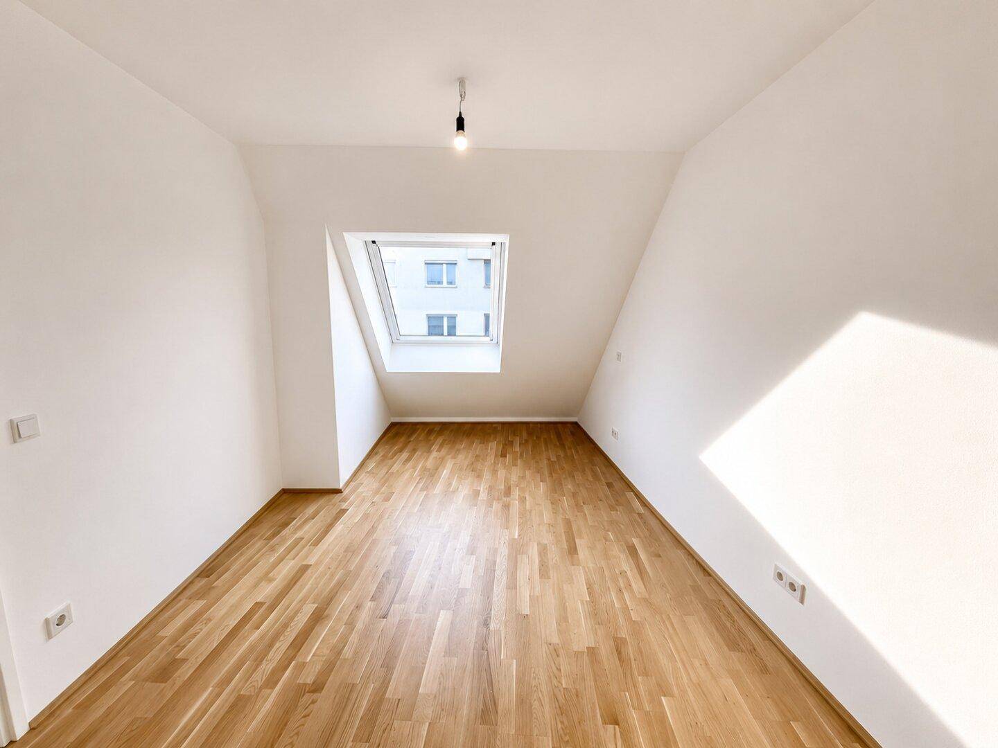 Helles Schlafzimmer im Dachgeschoss mit Holzboden und einem großen Dachfenster.