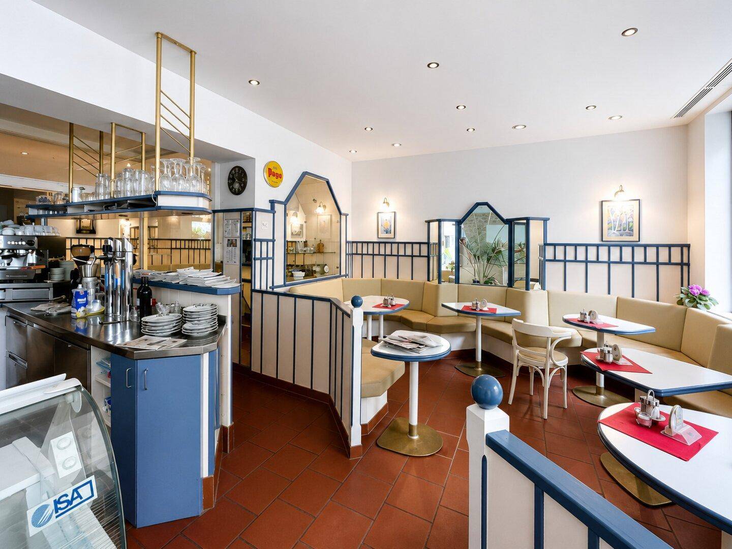 Geräumiger Café-Innenraum mit Theke, Sitzbereichen und Terrakotta-Boden, ideal für Gäste und Service.