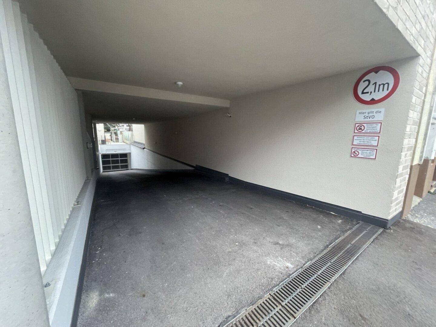 Einfahrt zu einer Tiefgarage mit Rampe, Höhenbegrenzung und Überwachungskamera.