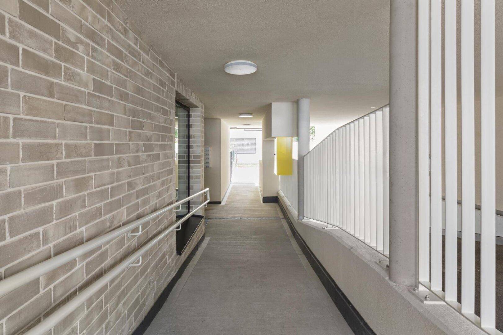 Barrierefreie Rampe mit Handläufen führt zum Eingang eines modernen Gebäudes.
