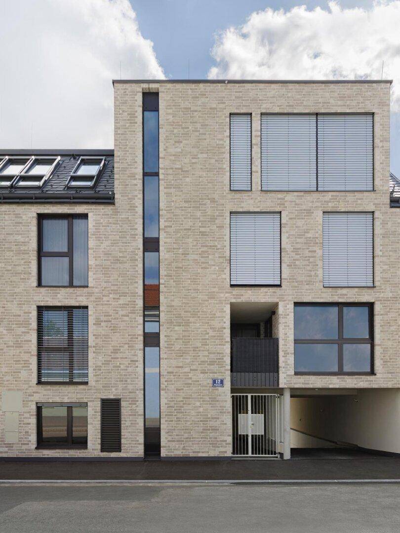 Moderne Fassade eines Mehrfamilienhauses mit heller Ziegelverkleidung und großen Fenstern.