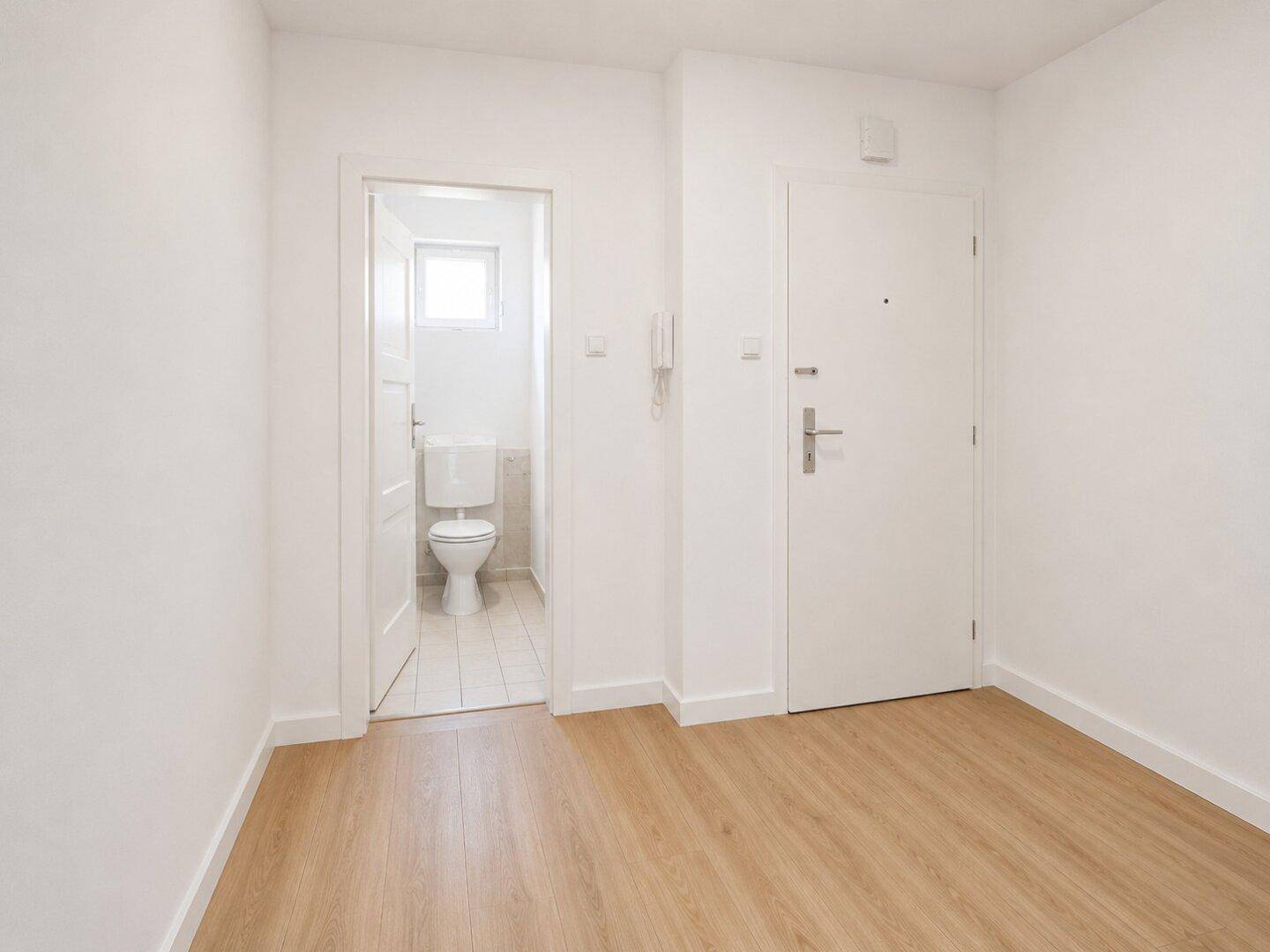 Renovierter Flur mit hellem Laminatboden und weißen Wänden, führt zu einem separaten WC.