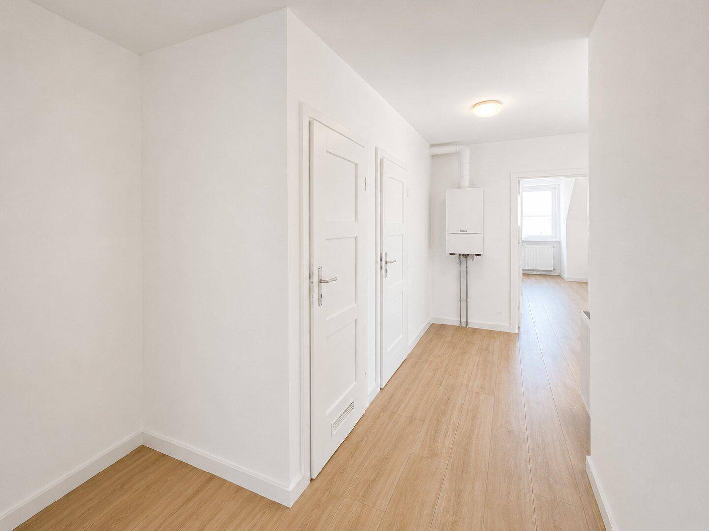 Renovierter Flur mit hellem Laminatboden, weißen Wänden und sichtbarem Heizkessel, führt zu weiteren Räumen.