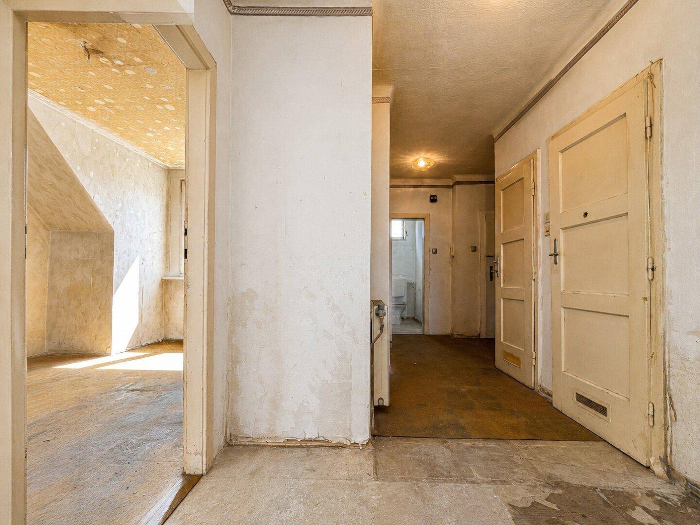 Unrenovierter Flur mit altem Bodenbelag und abgenutzten Wänden, führt zu weiteren Räumen und einem WC.