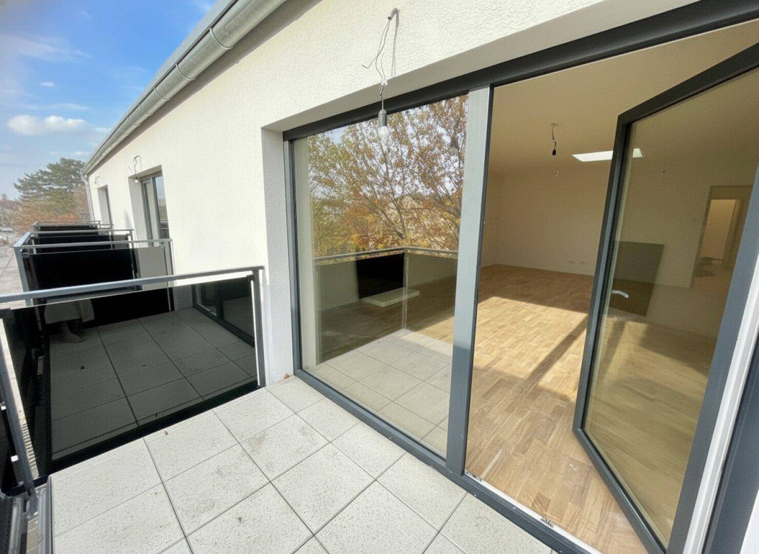 Balkon mit Fliesenboden und Glasgeländer, bietet Zugang zu einem hellen Innenraum.