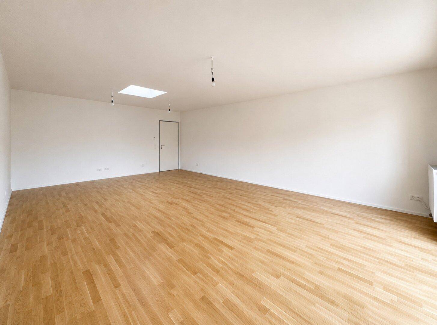 Geräumiges Zimmer mit hellem Holzparkett, weiß gestrichenen Wänden und einem Dachfenster.