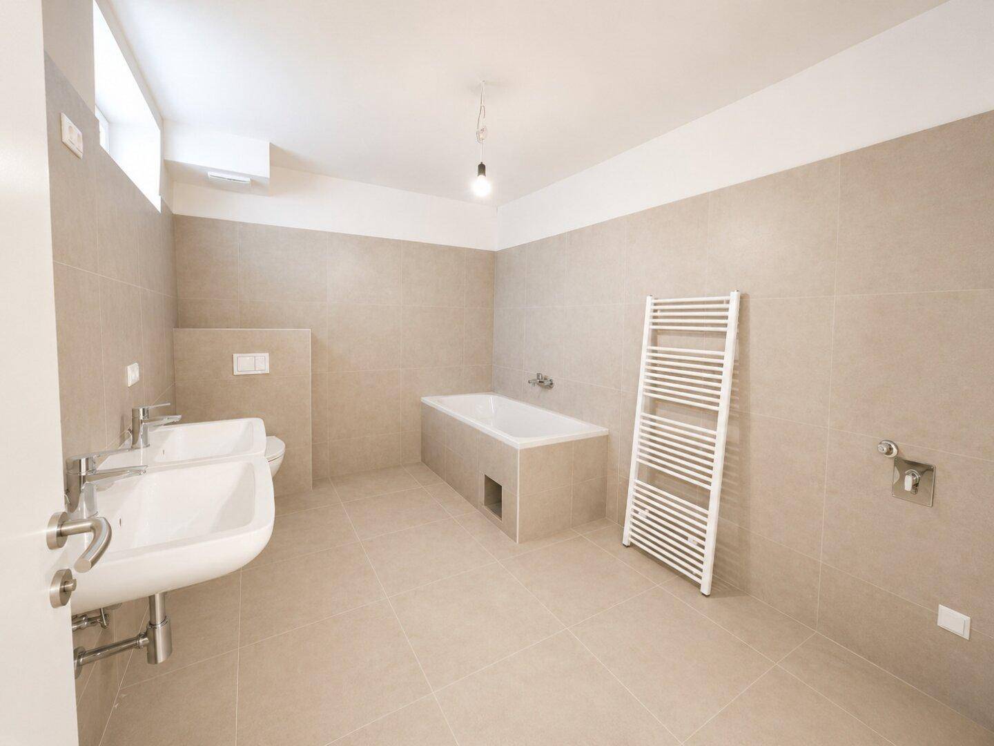 Modernes Badezimmer mit Doppelwaschbecken, Badewanne und beheiztem Handtuchhalter.
