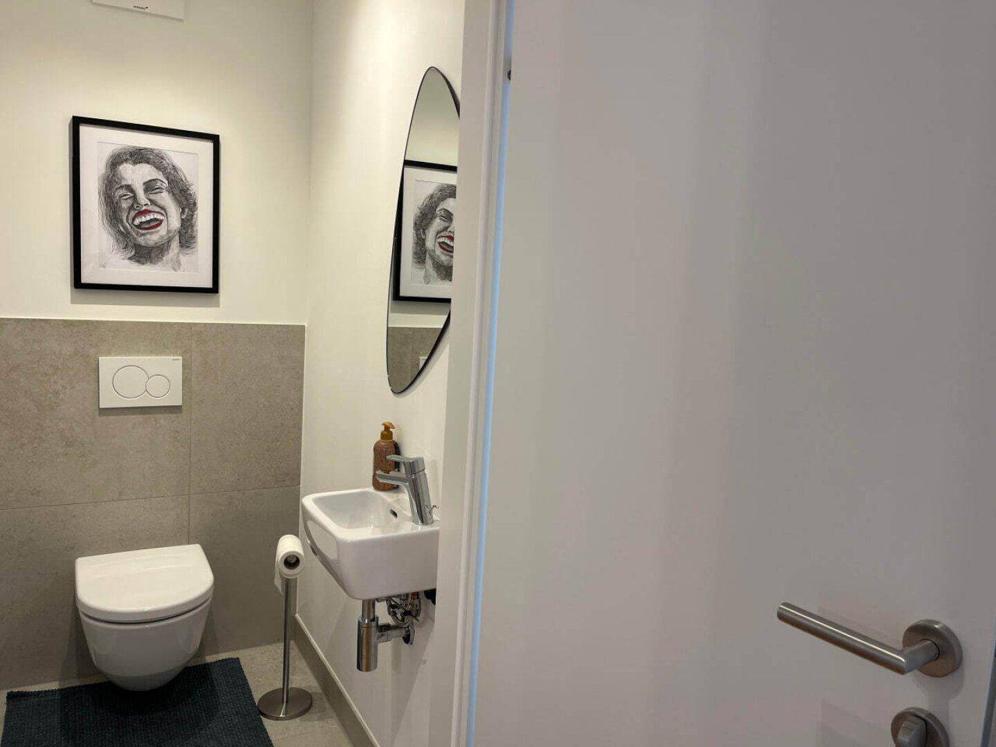 Modernes Gäste-WC mit wandhängender Toilette, kleinem Waschbecken und stilvollen grauen Fliesen.