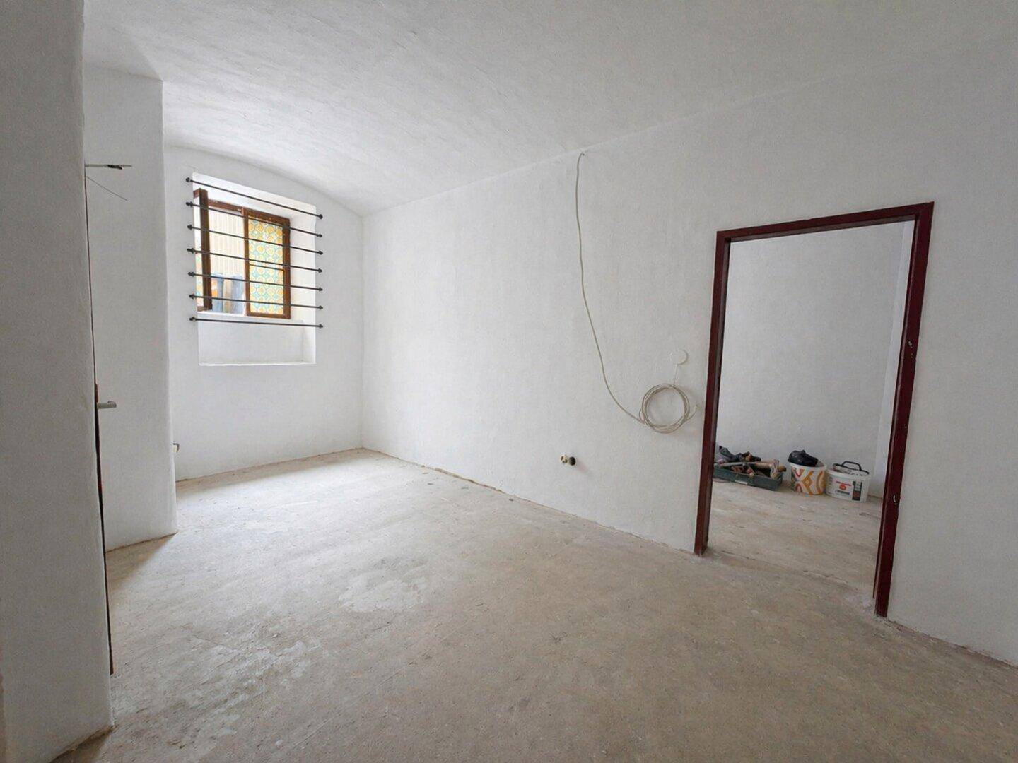 Leerer Raum mit weiß gestrichenen Wänden, einem Fenster mit Gitter und einem Türrahmen.
