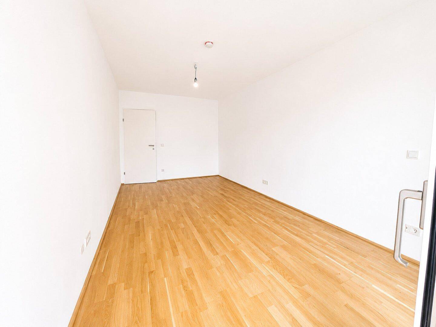 Leeres Zimmer mit Holzboden und weiß gestrichenen Wänden, bereit zur individuellen Einrichtung.