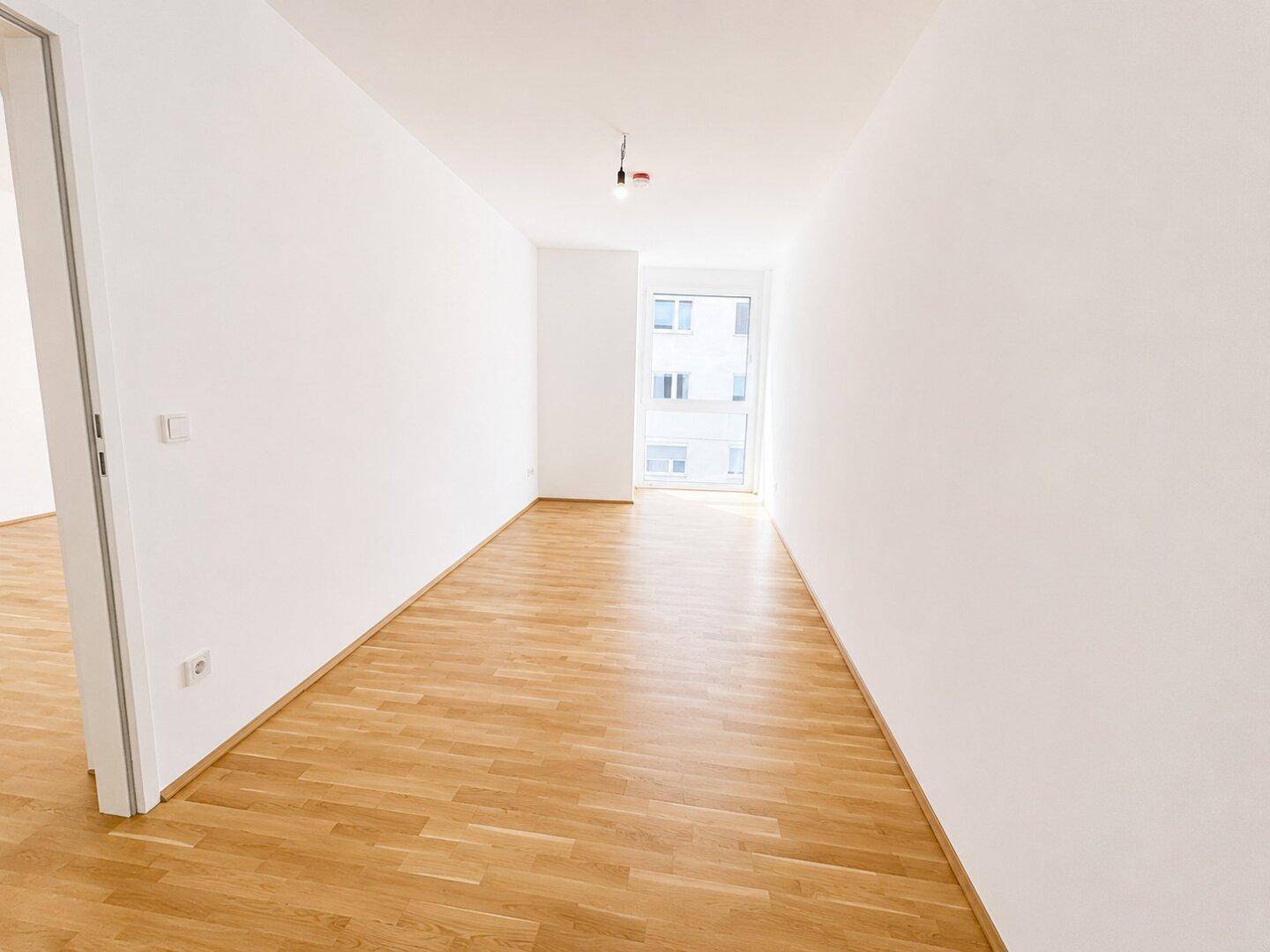 Langer, heller Flur mit Holzboden und Fenster am Ende, bietet vielseitige Nutzungsmöglichkeiten.
