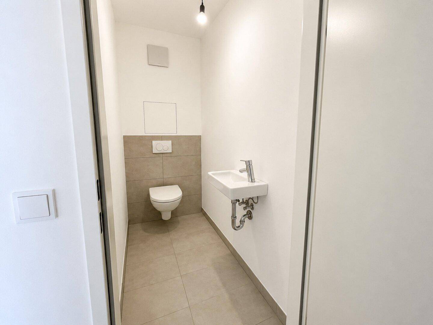 Separates WC mit wandhängender Toilette und kleinem Waschbecken.