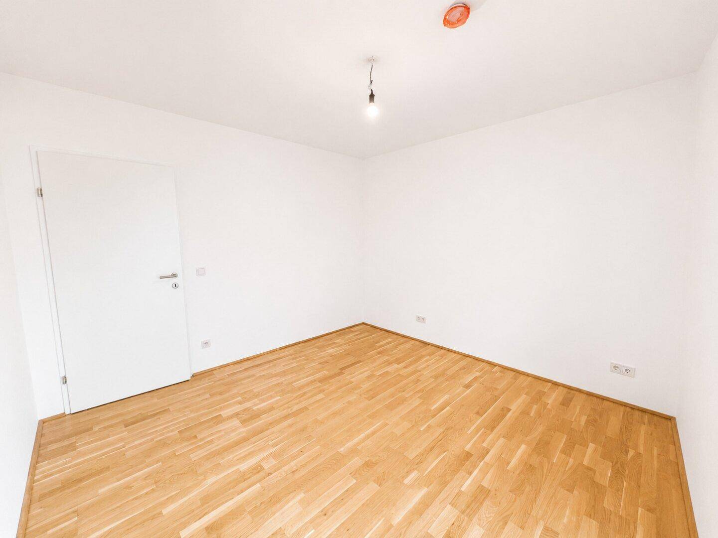 Leeres Zimmer mit Holzboden und weiß gestrichenen Wänden, ideal für ein Kinderzimmer.