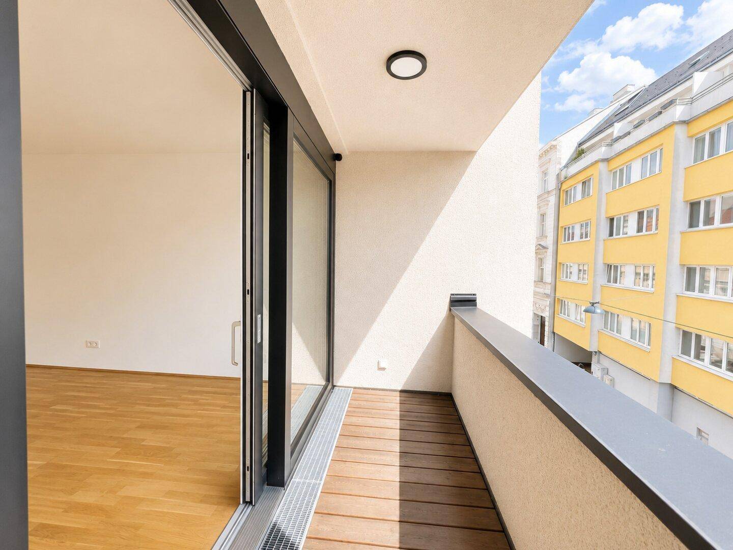 Langer Balkon mit Holzboden und Blick auf die umliegenden Gebäude der Stadt.