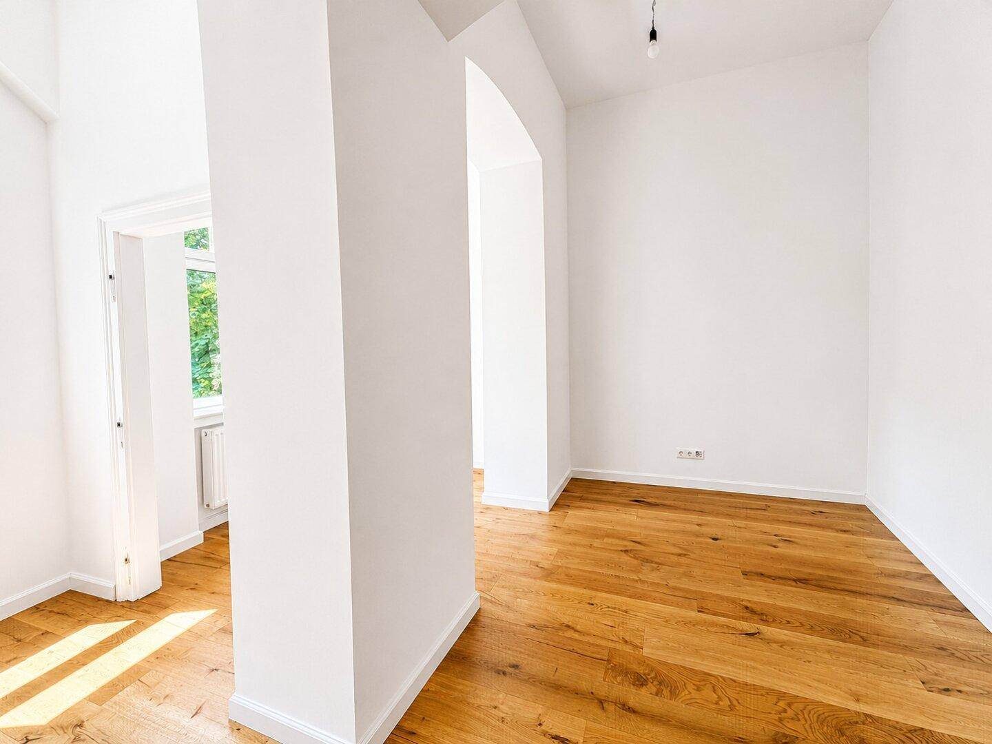 Heller, leerer Raum mit Holzboden und Durchgang zu einem weiteren Zimmer, bietet vielseitige Nutzung.