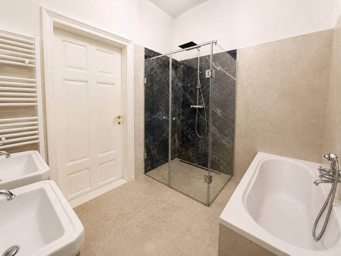 Modernes Badezimmer mit Badewanne, Duschkabine und zwei Waschbecken, in hellen Farbtönen gehalten.