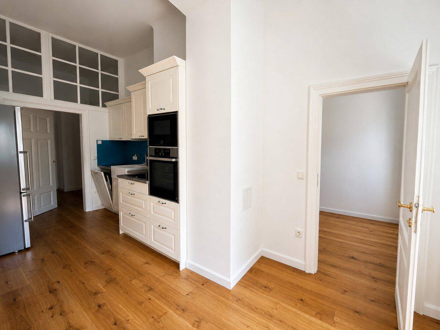 Helle Einbauküche mit modernen Geräten und Holzboden, offen zu angrenzenden Räumen.