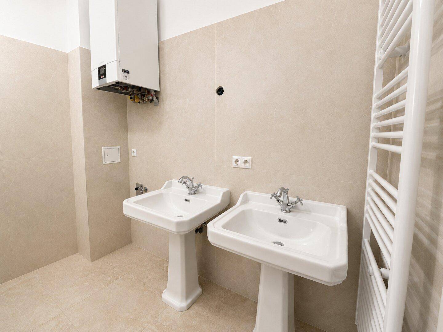 Helles Badezimmer mit zwei Standwaschbecken und Handtuchheizkörper, bereit für die Endmontage.