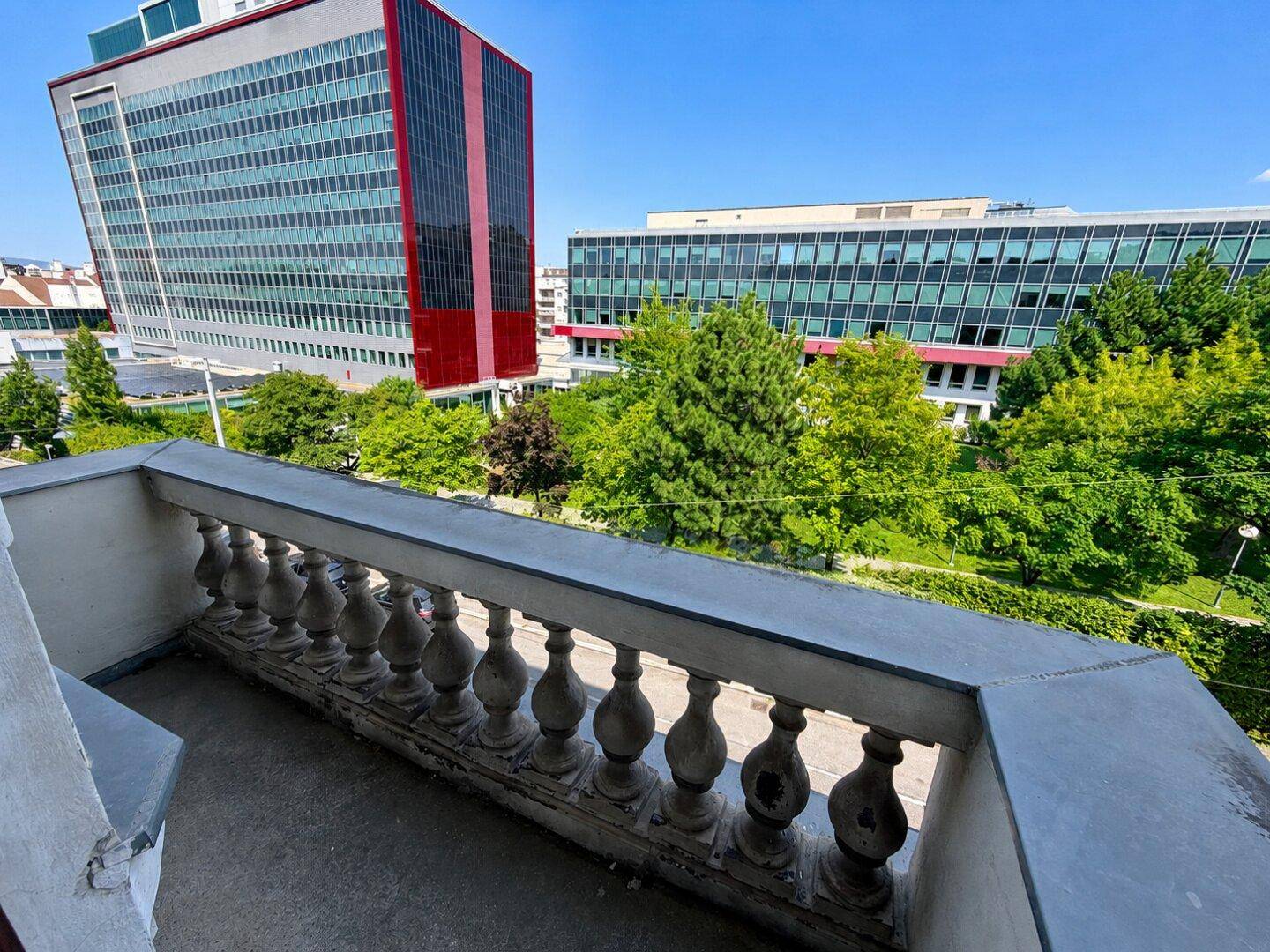 Balkon mit klassischem Geländer und Blick auf moderne Gebäude und grüne Bäume.