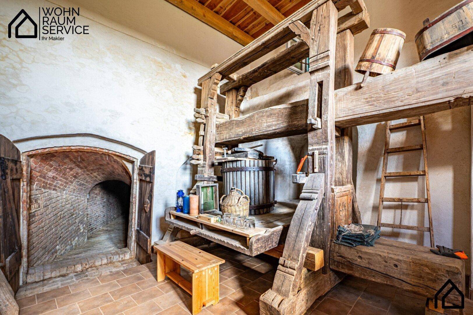 Historischer Weinkeller mit großer Holzpresse und traditionellen Fässern, rustikalem Charme.