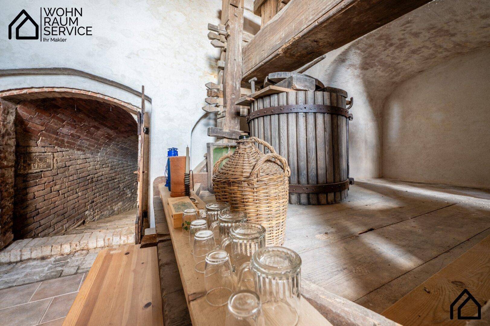 Detailansicht der alten Weinpresse mit Holzbottich und Gläsern in einem rustikalen Kellerraum.