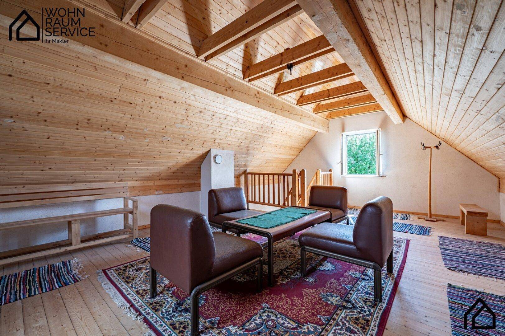 Gemütlicher Dachbodenraum mit Holztäfelung, sichtbaren Balken und Sitzgelegenheiten.