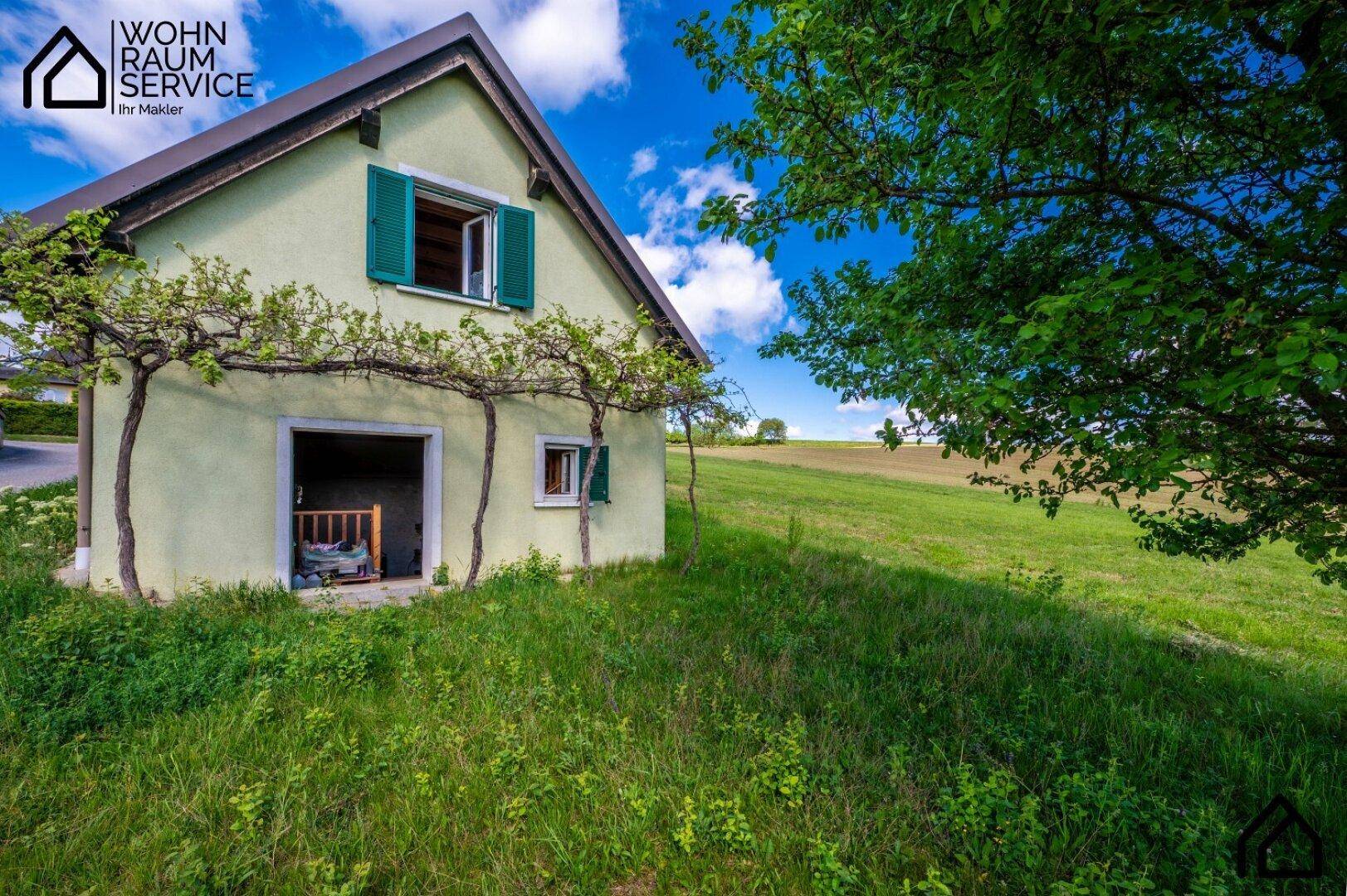Charmantes Landhaus mit grüner Fassade und Fensterläden, umgeben von üppiger Natur.