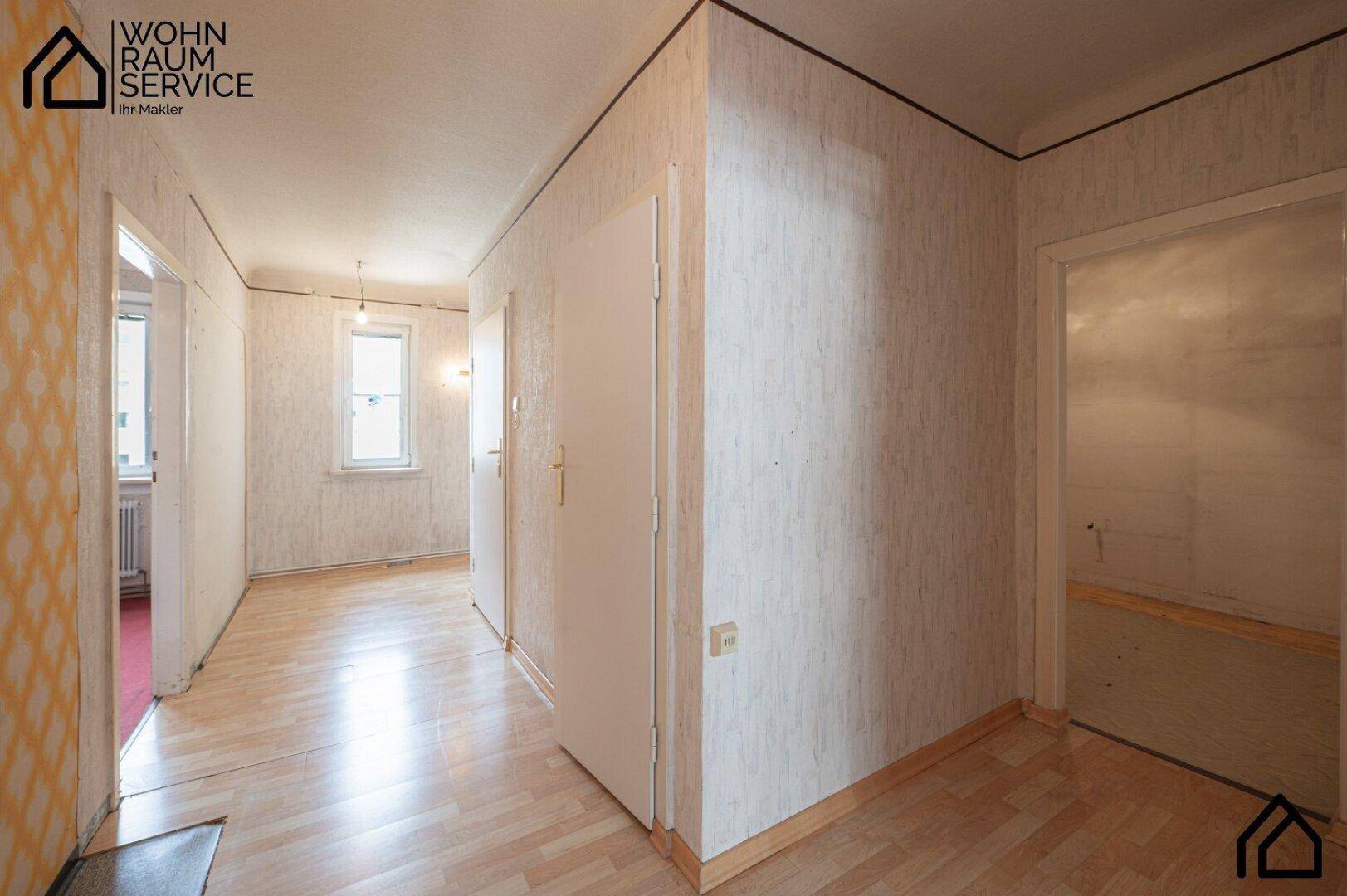 Heller Flur mit Holzfußboden und gemusterter Tapete, der zu verschiedenen Räumen führt.