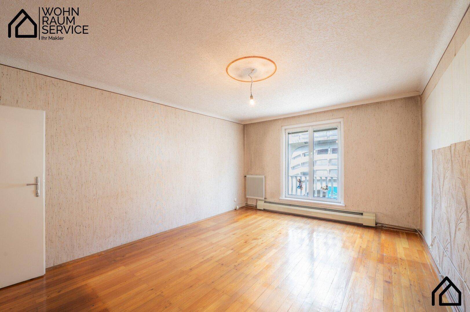 Leeres Zimmer mit Holzfußboden, heller Tapete und Fenster, bereit zur individuellen Gestaltung.