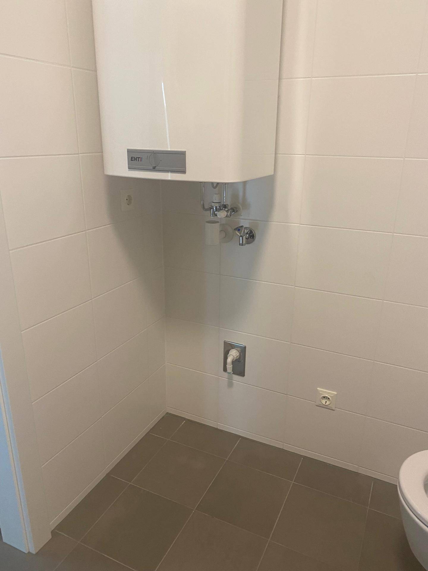 Ecke eines Raumes mit Warmwasserbereiter und weißen Fliesen an den Wänden.