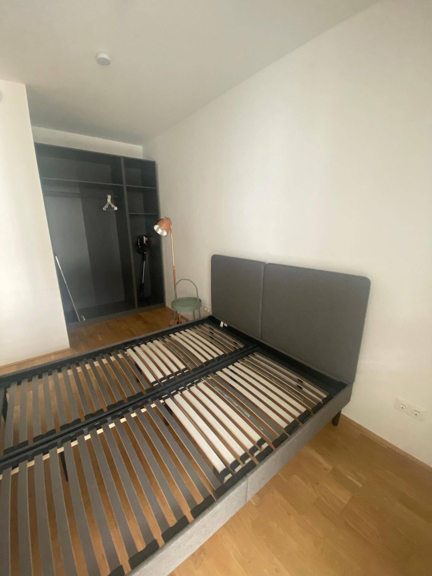 Schlafzimmer mit Bettrahmen, offenem Kleiderschranksystem und hellem Parkettboden.