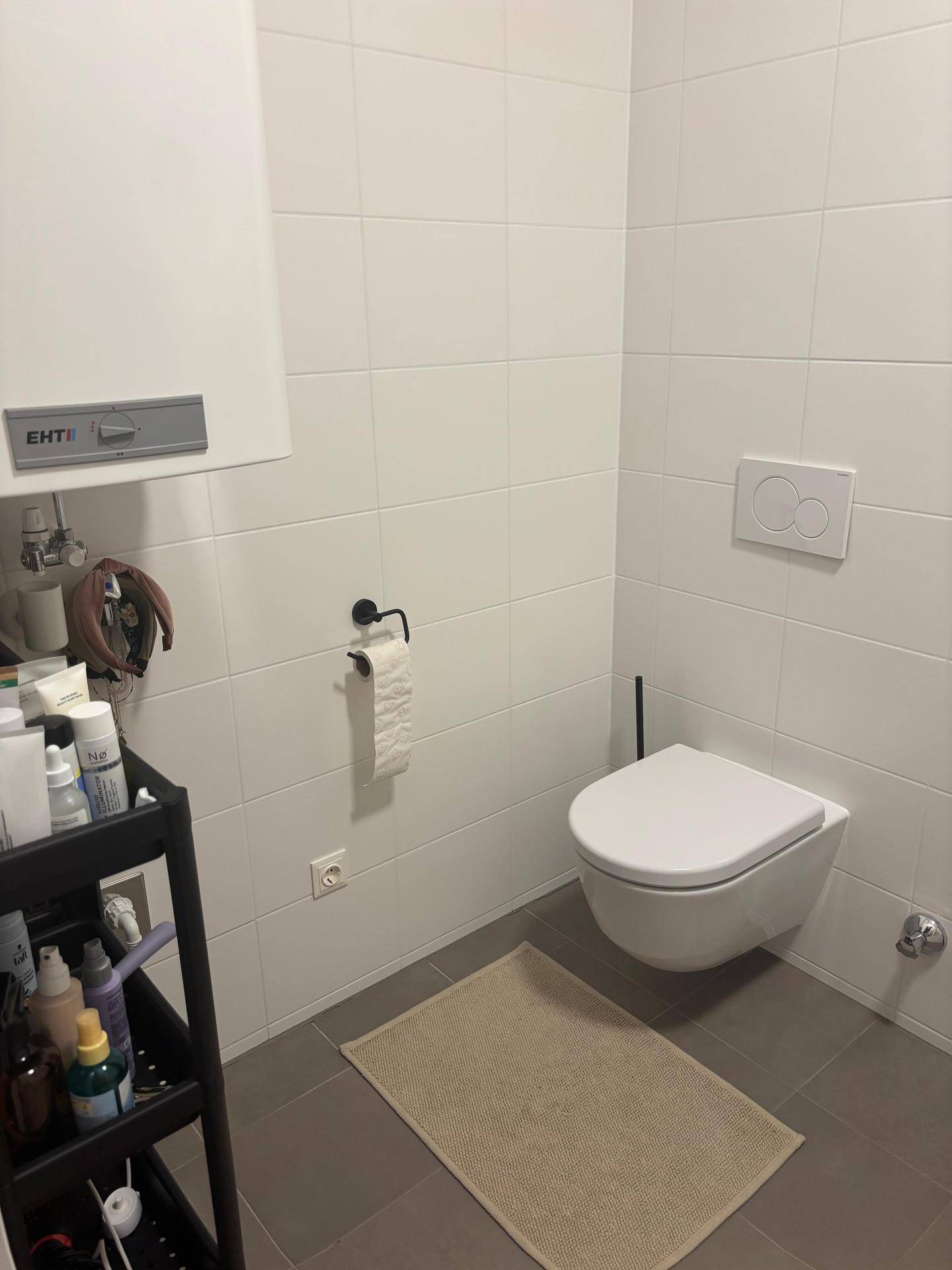 Separates WC mit wandhängender Toilette und einem Warmwasserbereiter an der Wand.