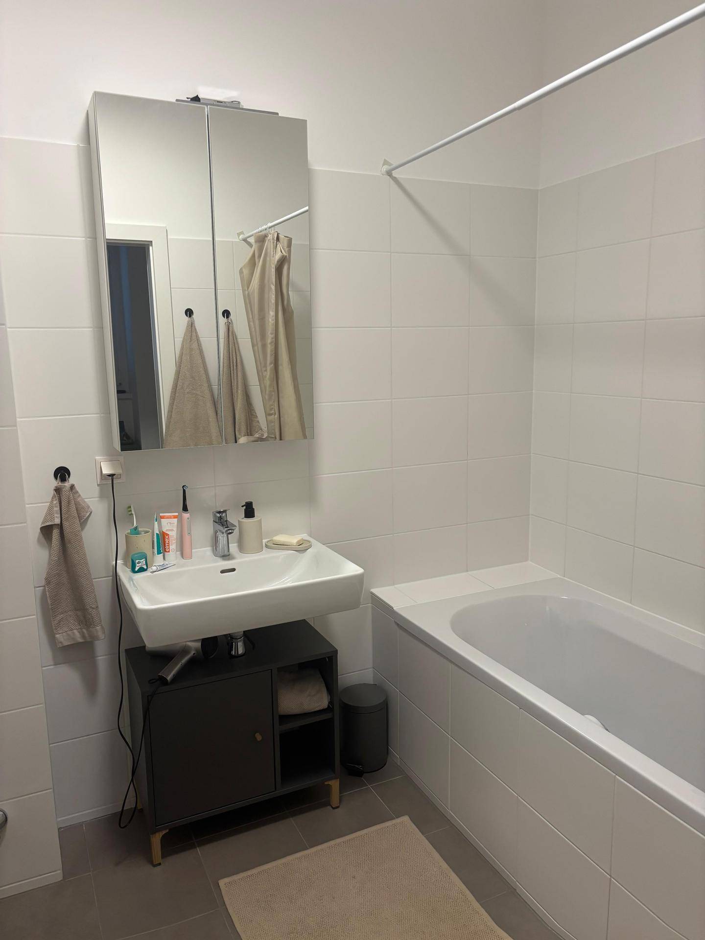 Helles Badezimmer mit Badewanne, Waschbecken und Spiegelschrank über dem Waschtisch.