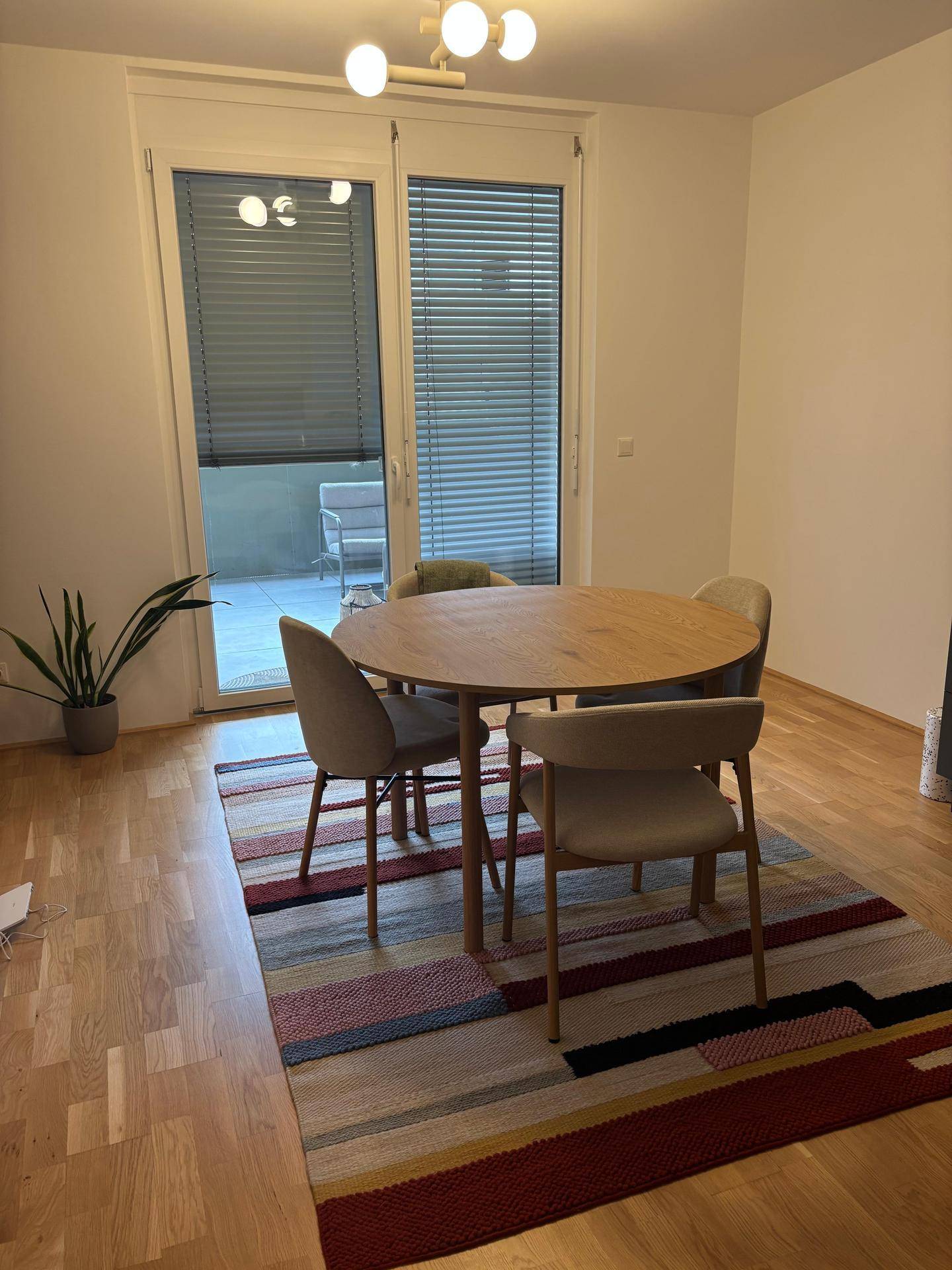 Gemütlicher Essbereich mit rundem Holztisch, Stühlen und Zugang zum Balkon.