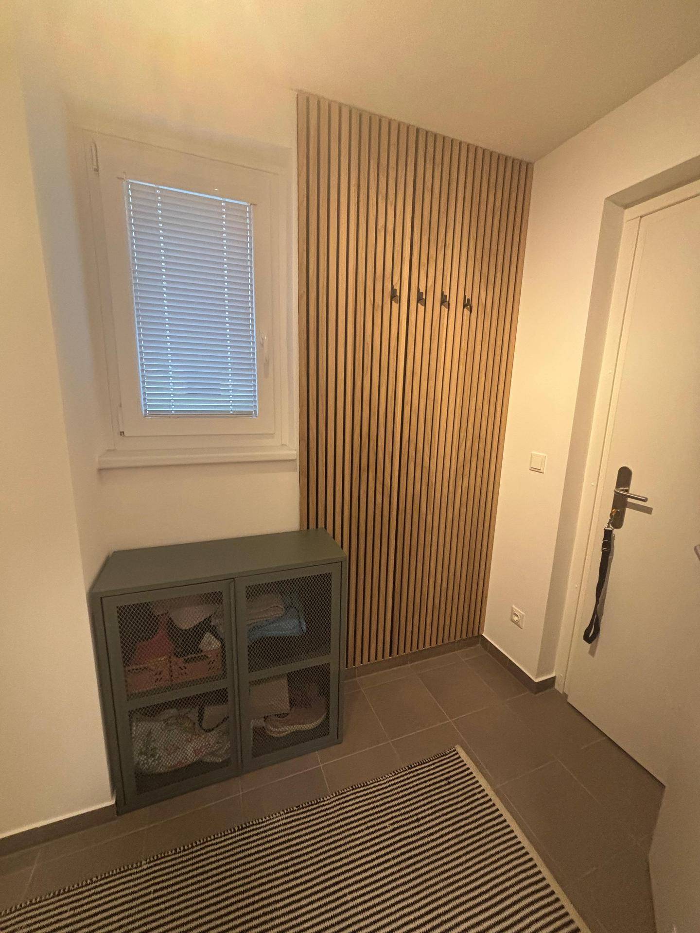 Eingangsbereich mit Fenster, Holzlamellenwand und einem Schuhschrank auf Fliesenboden.