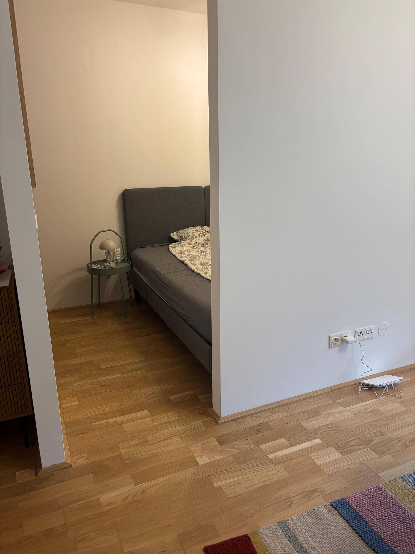Schlafzimmer mit Bett und hellem Parkettboden, angrenzend an einen weiteren Wohnbereich.