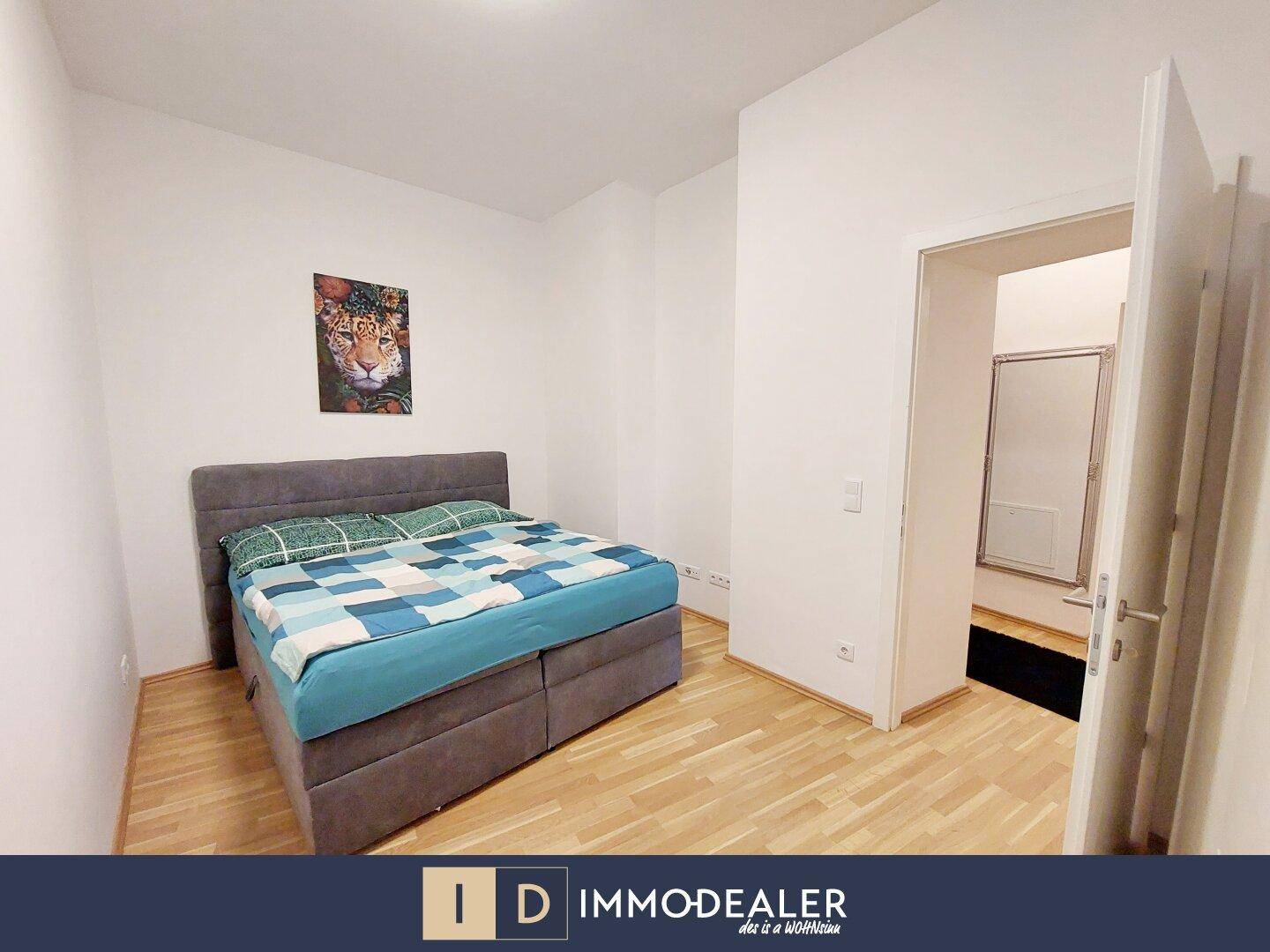 Schlafzimmer mit Doppelbett, Parkettboden und Zugang zu einem weiteren Raum.