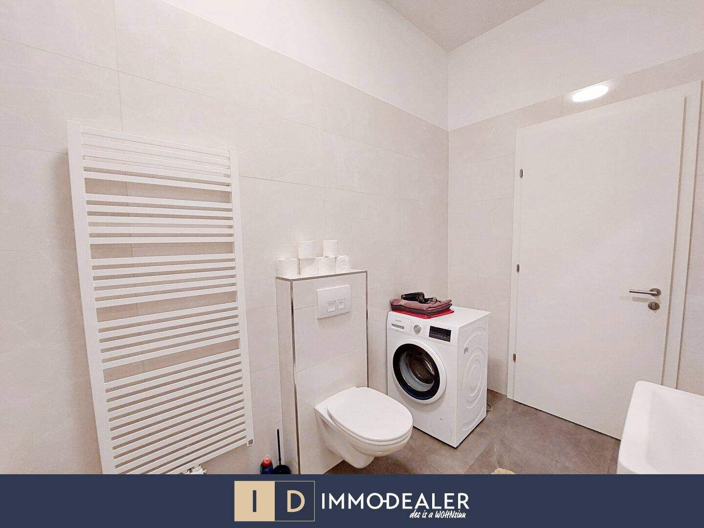 Badezimmer mit WC, Waschmaschine und beheiztem Handtuchhalter in hellen Fliesen.