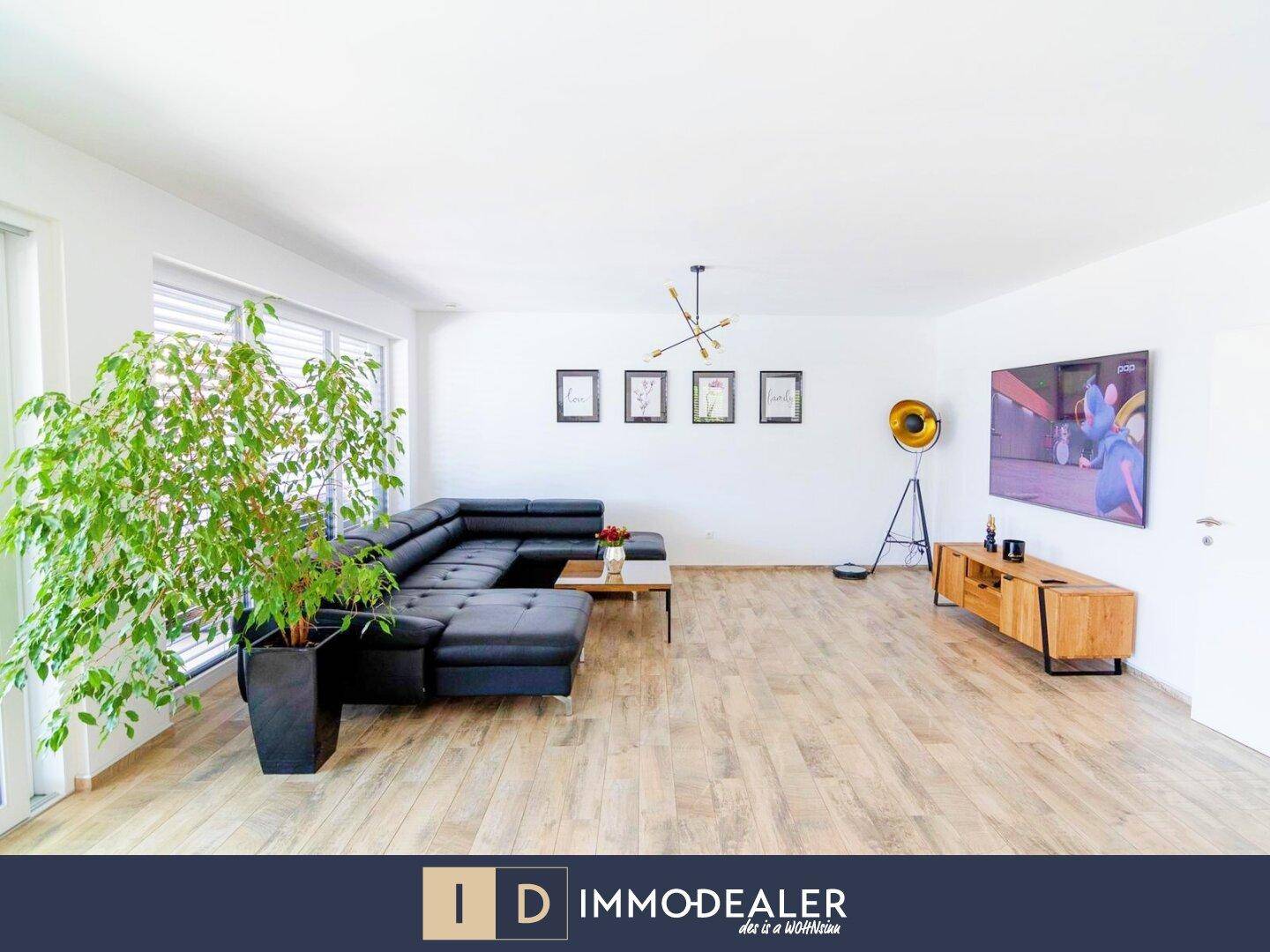 Helles Wohnzimmer mit modernem schwarzem Sofa, Holzboden und großer Zimmerpflanze.