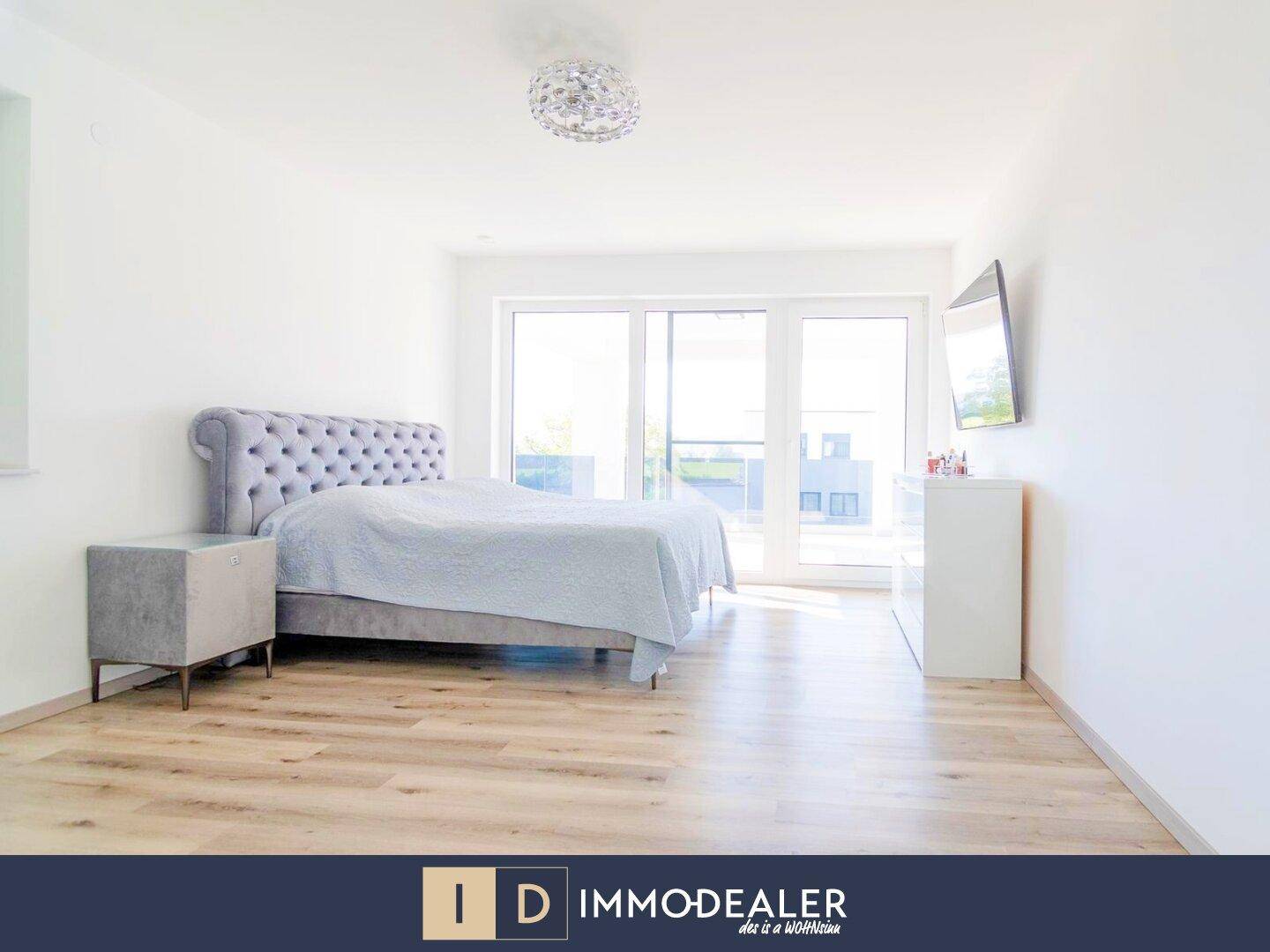Helles Schlafzimmer mit modernem Bett, Laminatboden und Zugang zu einem Balkon oder einer Terrasse.