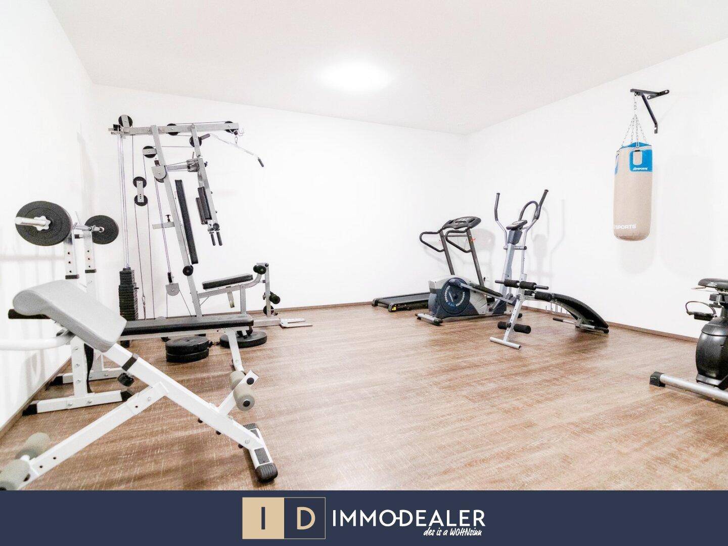 Geräumiger Fitnessraum mit verschiedenen Trainingsgeräten und hellem Holzboden.