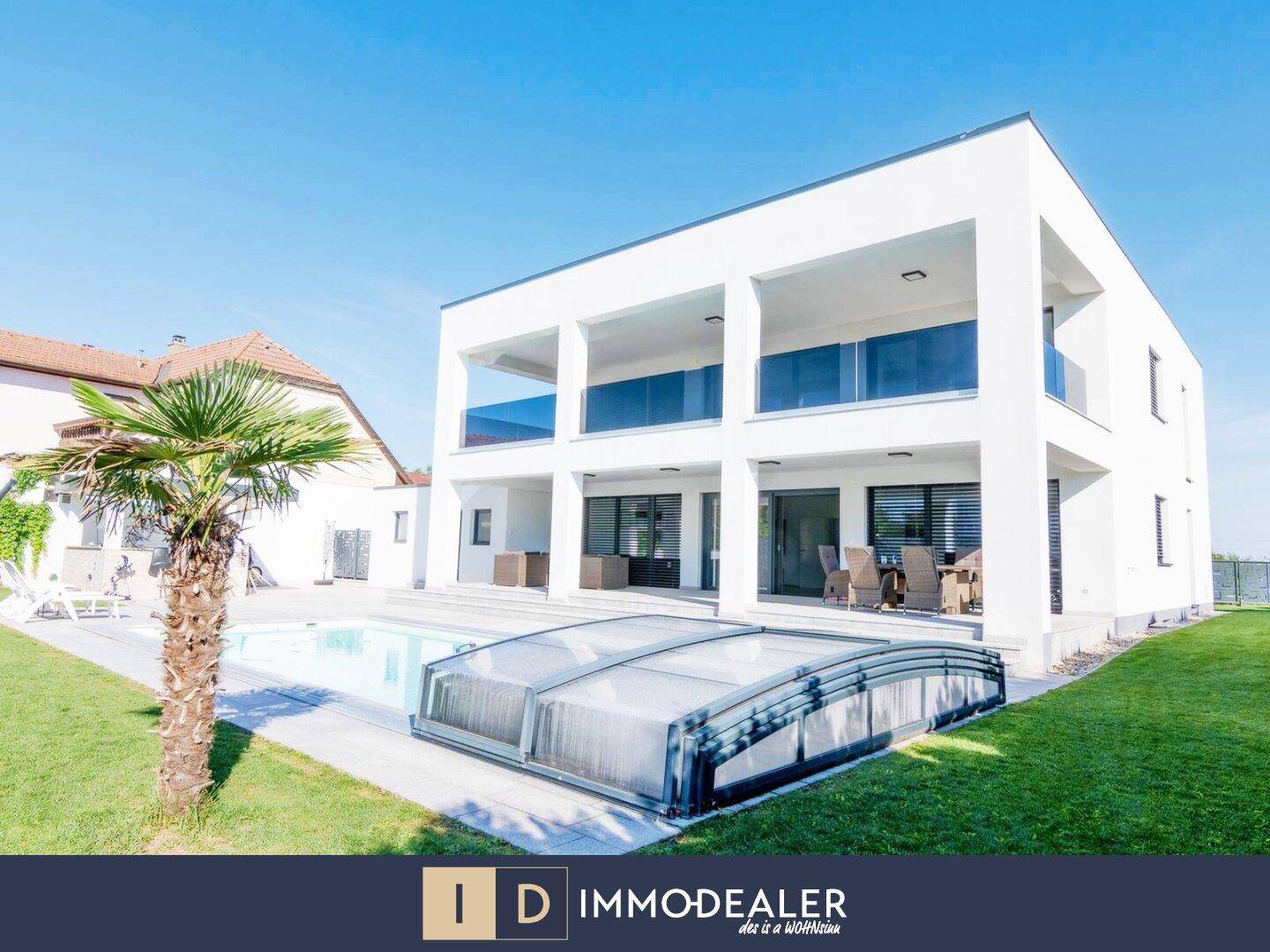 Moderne Villa mit großem Pool und Rasenfläche, umgeben von einer sonnigen Terrasse.