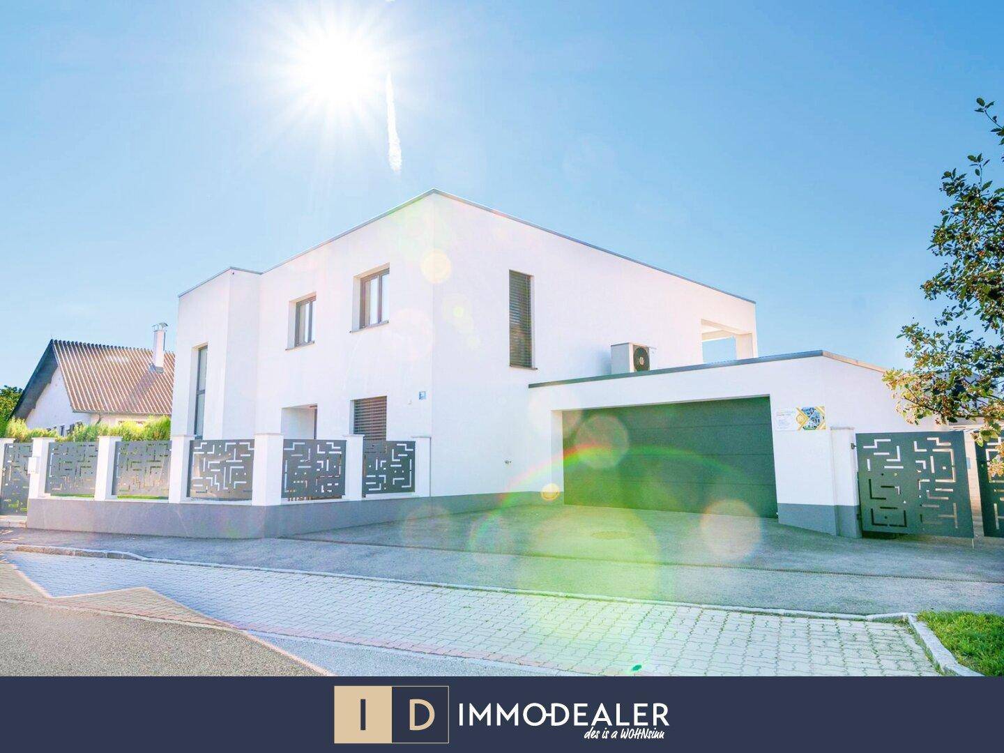 Moderne weiße Hausfassade mit integrierter Garage und dekorativem Zaun unter strahlendem Himmel.
